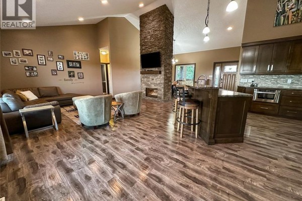Living room with a stone fireplace, large sectional sofa, and a kitchen island with stools. - Holars Haven Acreage, Spy Hill Rm No  152