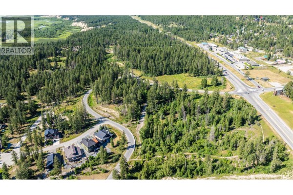 Aerial view of a wooded property with houses on a curved street, surrounded by trees and overlooking a highway and town. - Hot Springs Road Lot# 5056a, Fairmont Hot Springs
