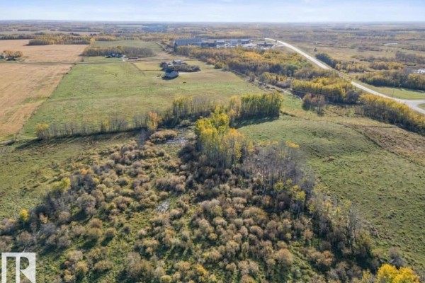 Aerial view of fields and trees, with some buildings and a highway visible in the distance under a blue sky. - Hwy 28 Rge Rd 424, Rural Bonnyville M D 