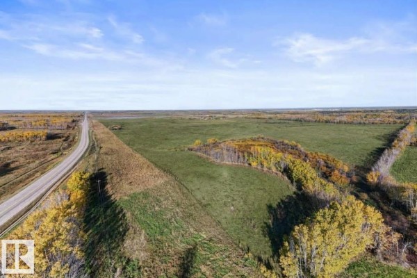 Aerial view of a large green field with a highway, trees, and a distant horizon under a blue sky. - Hwy 28 Rge Rd 424, Rural Bonnyville M D 