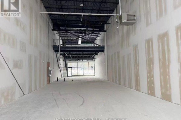 Long view of unfinished commercial interior with exposed ceiling beams and metal staircase. - 107 - 175 Melvin Robson Avenue, Aurora