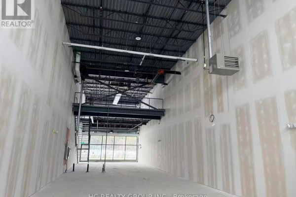 Interior view of unfinished commercial space with exposed ceiling beams, HVAC systems, and metal stairs. - 110 - 175 Melvin Robson Avenue, Aurora