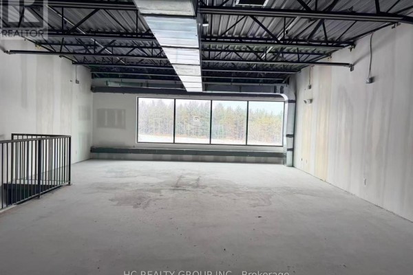 Interior view of unfinished commercial space with large windows showing a forest view, concrete floor and ceiling. - 110 - 175 Melvin Robson Avenue, Aurora