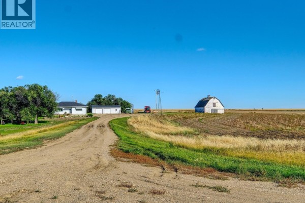 View of a white house, attached garage, red tractor, and a windmill. - Imlach Acreage, St  Andrews Rm No  287