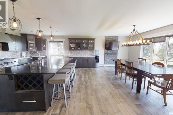 Open concept kitchen and dining area with dark cabinets, granite island, and a long wooden dining table. - Kindersley Acreage, Kindersley Rm No  290