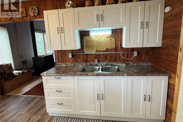 Close-up of a kitchen sink with white cabinets and wooden paneled wall. - Lac La Ronge Cabin Near Potato Point, Northern Admin District