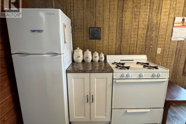 Kitchen corner with a white refrigerator, stove, and wooden paneled walls. - Lac La Ronge Cabin Near Potato Point, Northern Admin District
