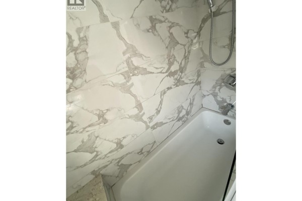 White bathtub with marble-patterned wall tiles and chrome showerhead. - Laneway House 3436 Tanner, Vancouver