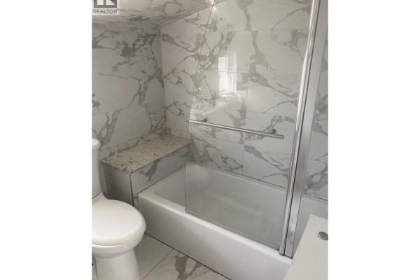 Bathroom with toilet, white bathtub, glass shower door, and marble-patterned tiles. - Laneway House 3436 Tanner, Vancouver