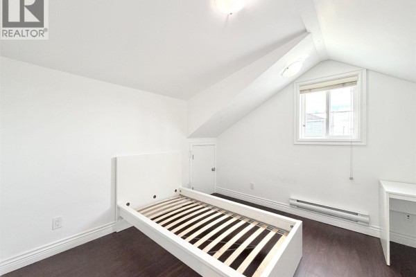 Attic bedroom with white walls, sloped ceiling, dark wood floor, white desk and bed frame. - 7456 Humm Street, Vancouver