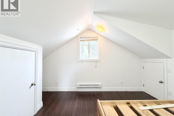 Attic bedroom with white walls, sloped ceiling, dark wood floor, white built-in desk, and two doors. - 7456 Humm Street, Vancouver