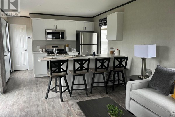 Open-concept kitchen with white cabinets, stainless steel appliances, and a breakfast bar with four stools. - Lkr026 - 1047 Bonnie Lake Camp Road, Bracebridge
