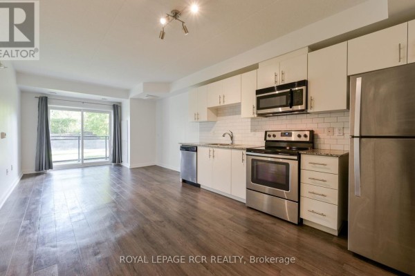 Apartment living area with sofa, armchair, coffee table on rug, and open-concept kitchen. - Ll02 - 25 Kay Crescent, Guelph