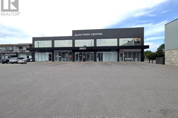 Wide shot of the commercial building exterior and surrounding asphalt parking area. - Ll2 - 2920 Dufferin Street, Toronto