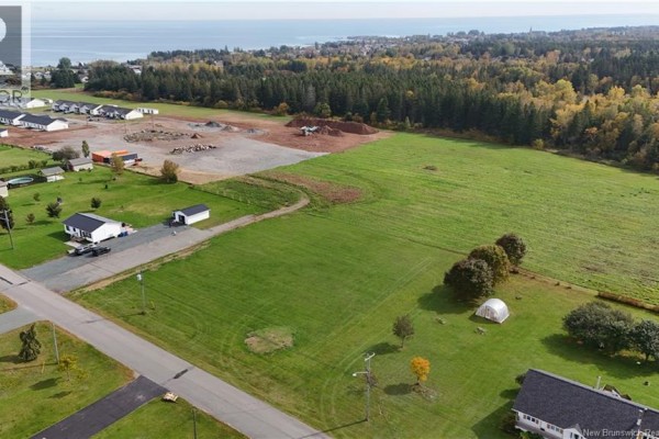 Aerial view of grassy lots, some with houses and construction activity, bordering a forest and the sea. - Lot 1 Cormier, Petit Rocher