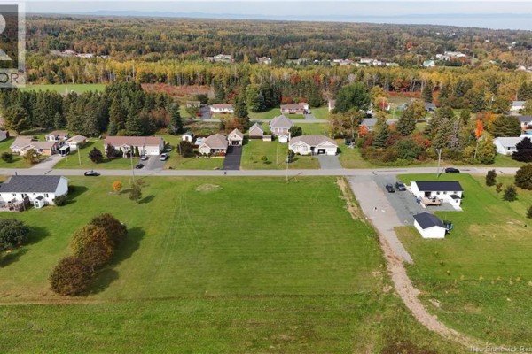 Aerial view of houses on a street facing a large, flat, green, grassy lot. - Lot 1 Cormier, Petit Rocher