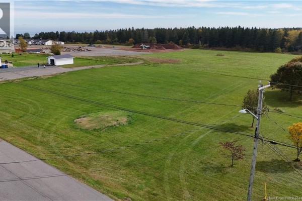 Aerial view of a vast grassy field with houses, trees, and a small white shed in the distance. - Lot 1 Cormier, Petit Rocher