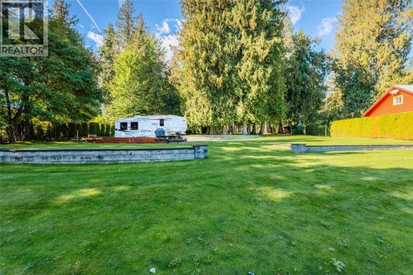 A spacious lawn area with a trailer on a wooden deck, surrounded by trees and a red-sided building. - Lot 1 Lower Six Mile Road, Nelson