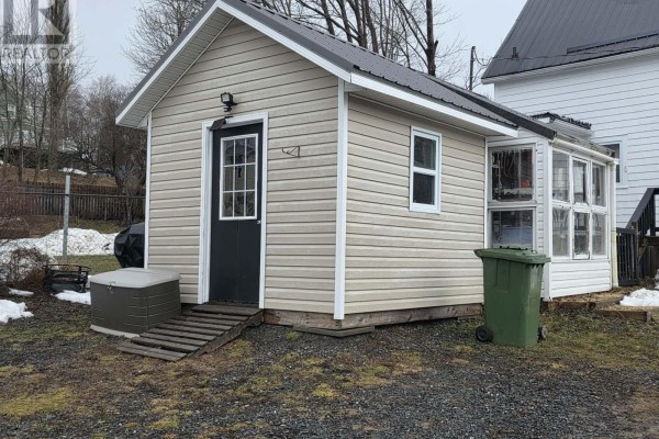 Exterior view of a small outbuilding with a black door and windows, surrounded by gravel. - Lot 10 88 St. Andrews Street, Pictou