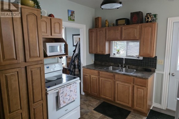 Kitchen with wooden cabinets, dual sinks, and a window, featuring beige walls and tile flooring. - Lot 10 88 St. Andrews Street, Pictou