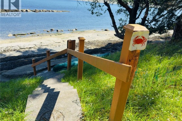 Concrete stairs with wooden handrails leading down to a grassy area and a shoreline with a kayak. - Lot 10 Driftwood Dr, Mudge Island