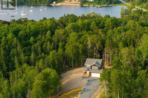 Rear exterior of a dark grey house with a large wooden deck and multiple windows. - Lot 102 Peggys Cove Road, French Village