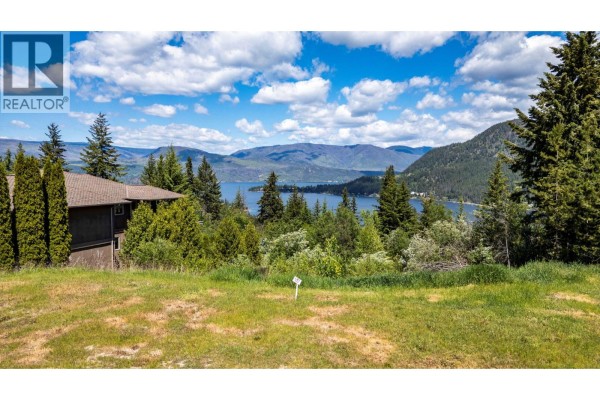 A house with a brown roof sits on a wooded slope overlooking a wide blue lake. - Lot 117 Golf Course Drive, Blind Bay