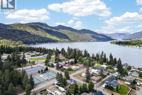 A playground with swings, slides, and climbing structures sits on a grassy lawn surrounded by trees. - Lot 14 Caitlin Road, Christina Lake