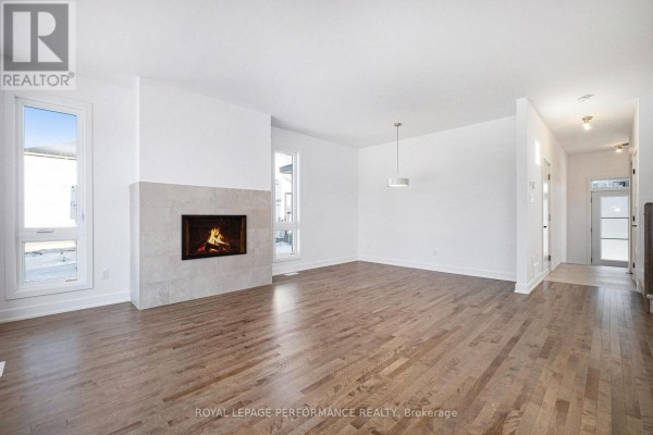 Living room with hardwood floors, white walls, a modern fireplace with a stone surround, and large windows. - Lot 149 Bourdeau Boulevard, The Nation