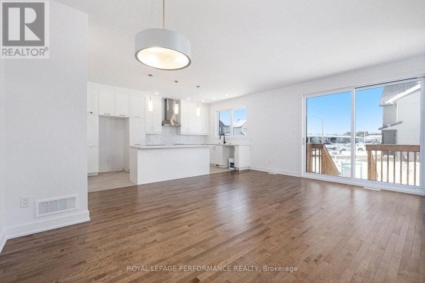 Open concept living area with hardwood floors, white kitchen cabinets, island, and sliding glass doors to a wooden deck. - Lot 149 Bourdeau Boulevard, The Nation
