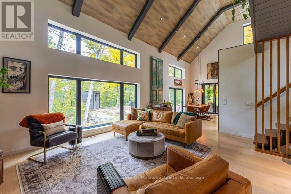 Living room with a leather sectional, fireplace, and large windows overlooking autumn trees. - Lot 18 - 113 Gryffin Bluffs Lane, Huntsville