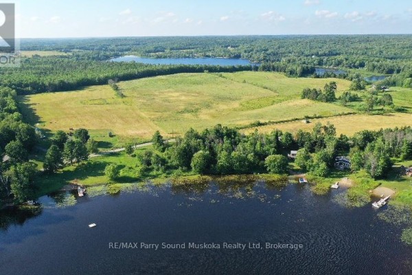 Overhead view of a dark blue lake with a grassy shoreline, scattered trees, and a few small docks. - Lot 18 Concession 3 Street, Seguin