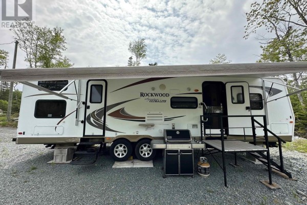 Recreational vehicle with extended awning, outdoor grill, propane tank, and stairs on a gravel pad. - Lot 19 7 Highway, Goldenville