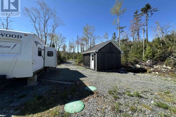 View of an RV and a small dark wooden shed with a white door on a gravel lot. - Lot 19 7 Highway, Goldenville
