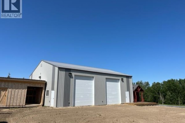 Silver workshop with two white garage doors, a small wooden shed, and trees in background. - Lot 2 - 70539 Rng Rd 250, Rural Greenview No  16, M D  Of