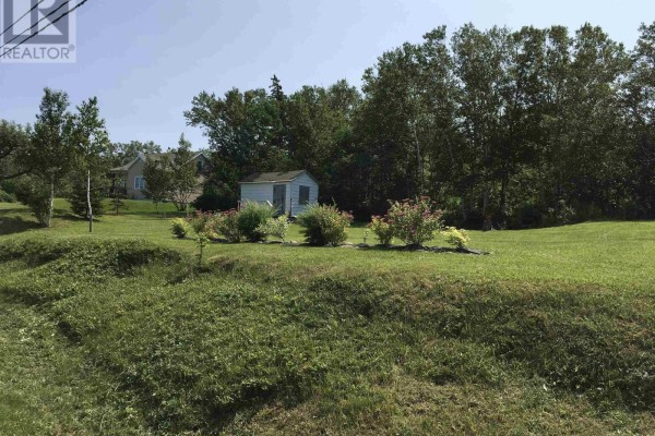 A white shed is centered in a grassy yard with trees and bushes in the background. - Lot 2 Cabot Trail, La Prairie