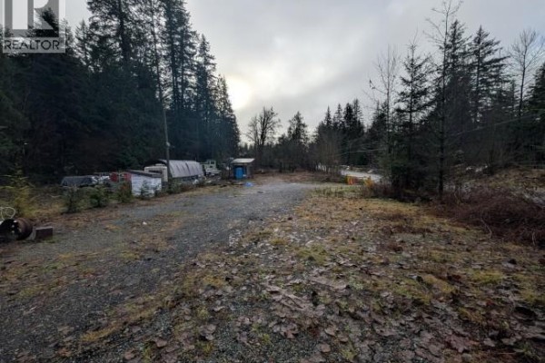 Gravel area with overgrown vegetation, surrounded by trees and trailers in the distance. - Lot 2 Squamish Valley Road, Squamish