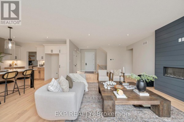 Living room with light wood floors, grey feature wall with fireplace, and multiple seating areas. - Lot 2 Sunningdale Court, London North