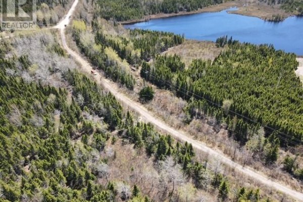 Aerial perspective of a long, straight dirt road cutting through a forest with power lines and a lake. - Lot 2 Third Pond, Glovertown
