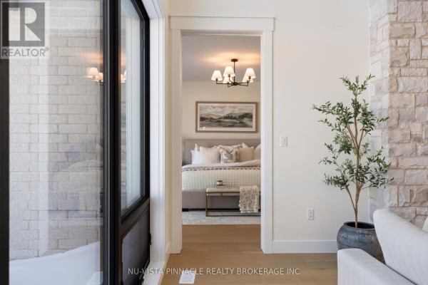 View through a doorway into a bedroom with a king-size bed and landscape artwork above the headboard. - Lot 20 Harvest Lane, Thames Centre