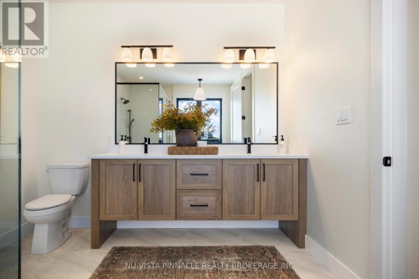 A double vanity bathroom with a large rectangular mirror, wood cabinets, and a toilet to the left. - Lot 20 Harvest Lane, Thames Centre