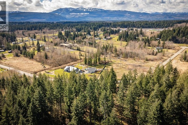 Aerial view of houses and cleared land surrounded by forest, with mountains in the background. - Lot 21 Oyster River Way, Black Creek