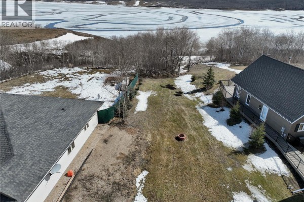 View of a grassy lot with scattered snow, bordered by homes, trees, and a green fence. - Lot 21 Pelican Landing, Lake Of The Prairies