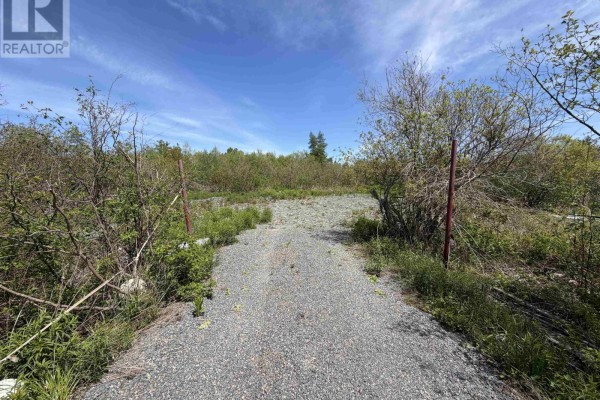A gravel driveway is framed by brush and red metal posts against a wooded background. - Lot 22-3 Wallace Bridge Station Road, Wallace River West
