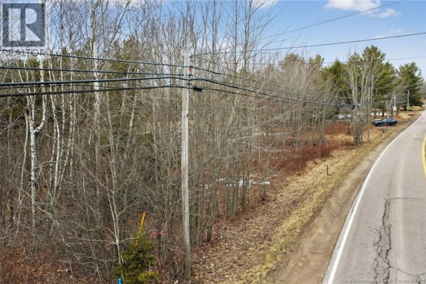 Aerial view of a wooded lot with a winding road and distant water under a cloudy sky. - Lot 26-03 Dover Road, Dieppe