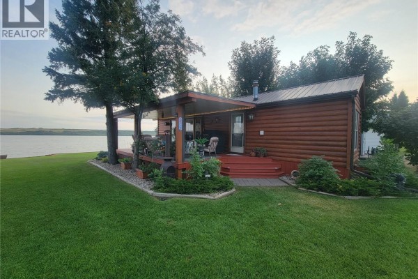 Exterior view of a mobile home with a covered wooden deck, outdoor seating, and landscaping. - Lot 3 Lakeshore Drive, Eye Hill Rm No  382