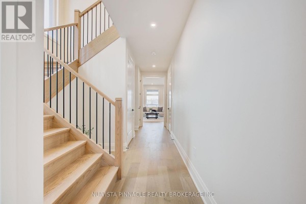 Hallway with light wood floors, a wooden staircase with black railings, and doorways to other rooms. - Lot 35 Virtue Drive, London South
