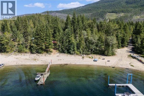 View from the water looking at a sandy beach, dock, and forested shoreline. - Lot 4 Queest N. Bay, Sicamous