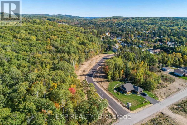 Aerial view of a residential area with homes, a paved road, and a lake surrounded by trees. - Lot 40 Yantha Crescent, Madawaska Valley