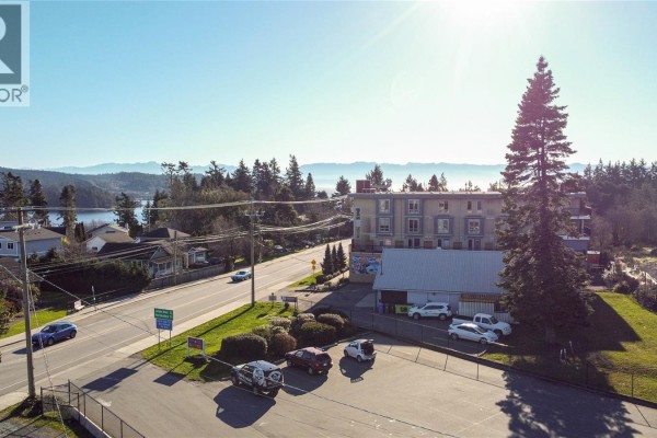 View of a street with a hotel and nearby buildings, with mountains in the background. - Lot 5 West Coast Rd, Sooke